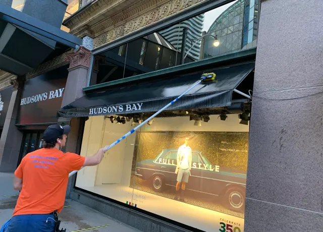 Worker cleaning Hudson's Bay store window display.