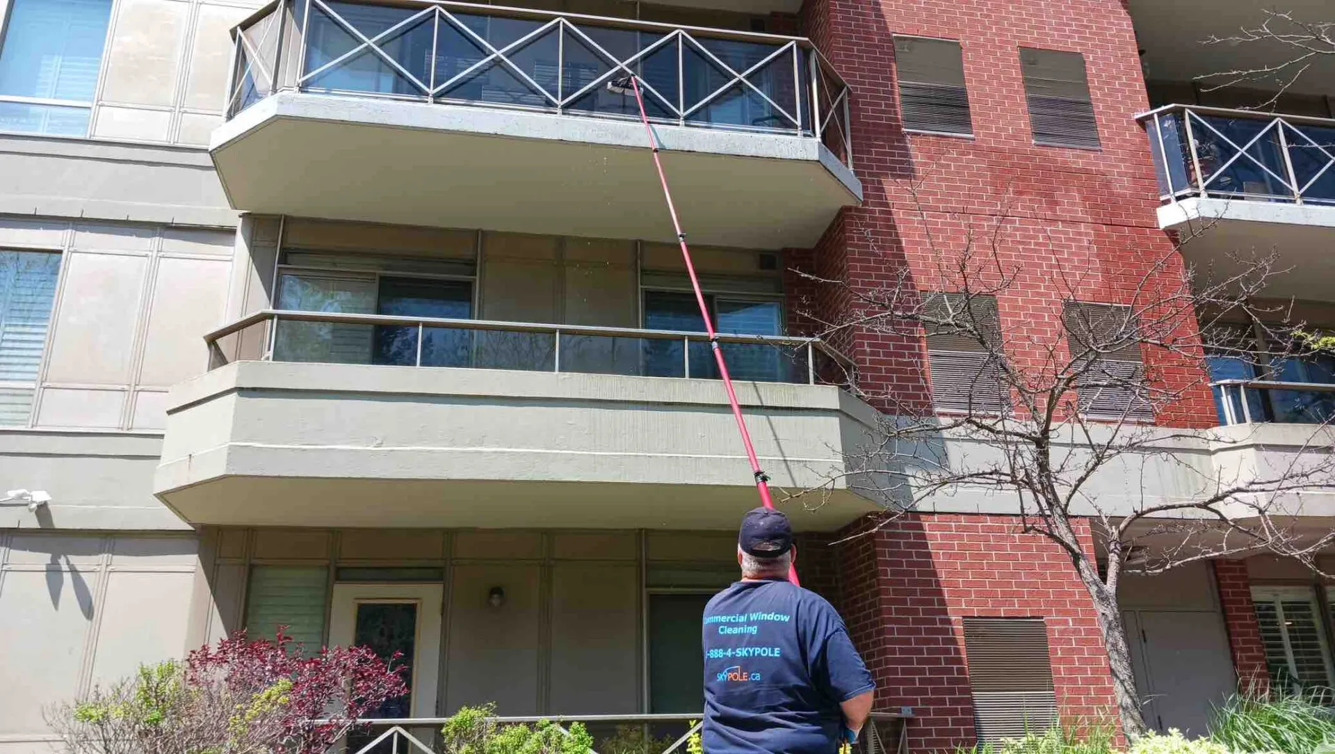 Man cleaning apartment windows with long pole.