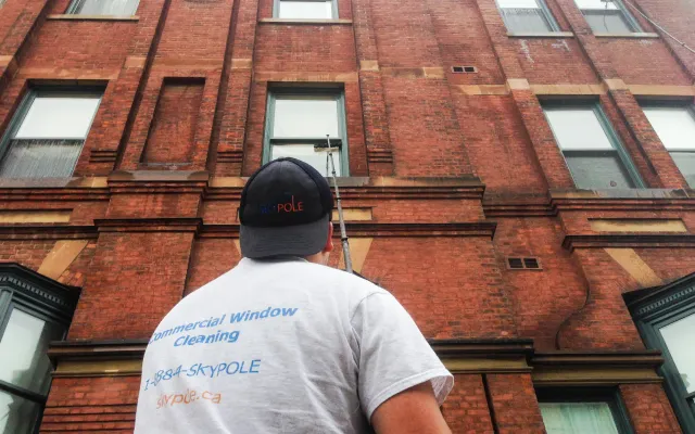 Window cleaner examining brick building exterior.