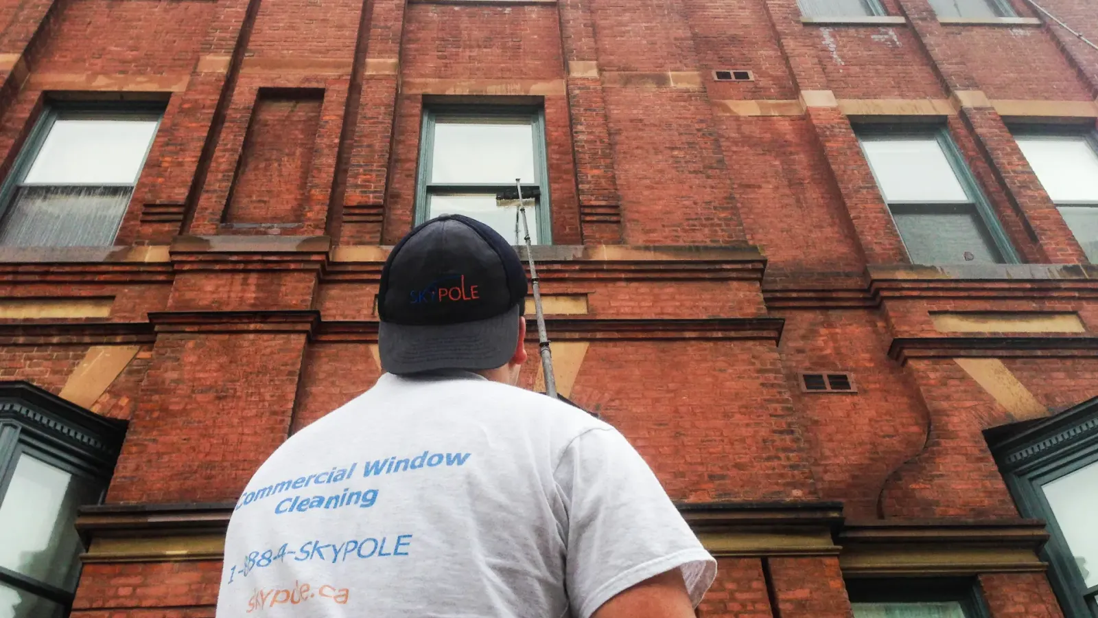 Window cleaner examining brick building exterior.