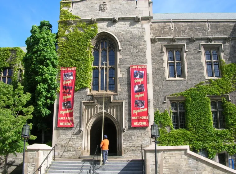 Person near ivy-covered Hart House entrance with banners.