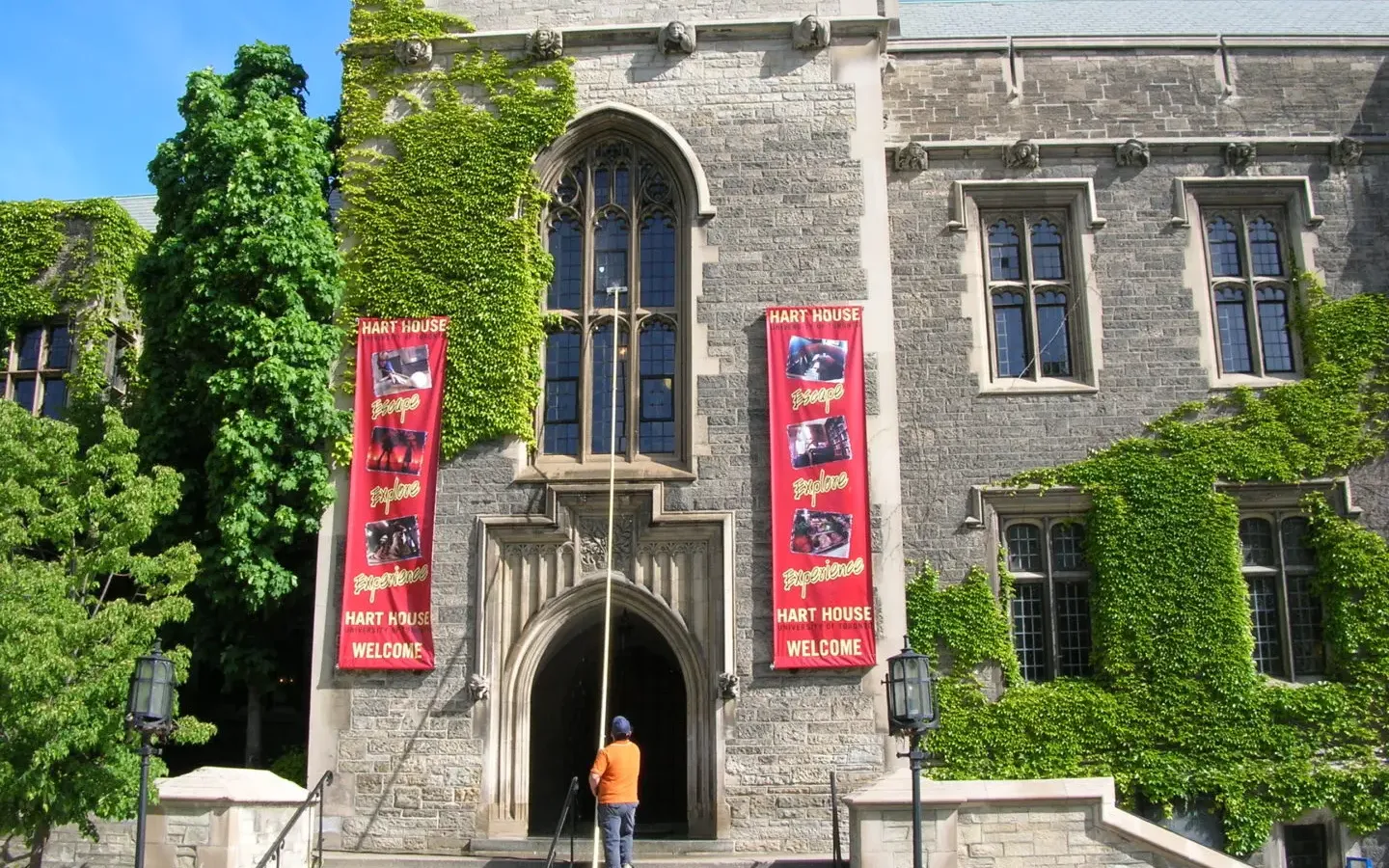Person near ivy-covered Hart House entrance with banners.