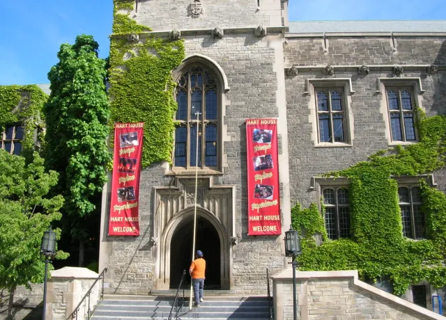 Person near ivy-covered Hart House entrance with banners.