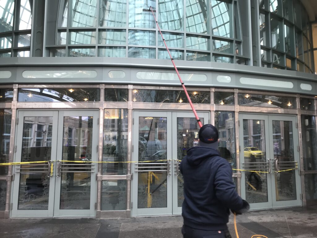 Worker cleaning glass building entrance with long tool