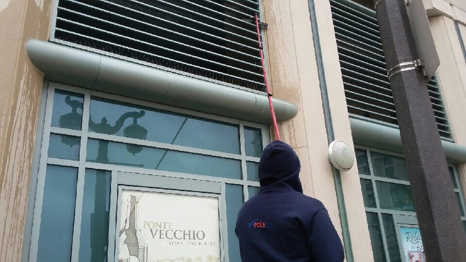 Person cleaning building facade with telescopic pole