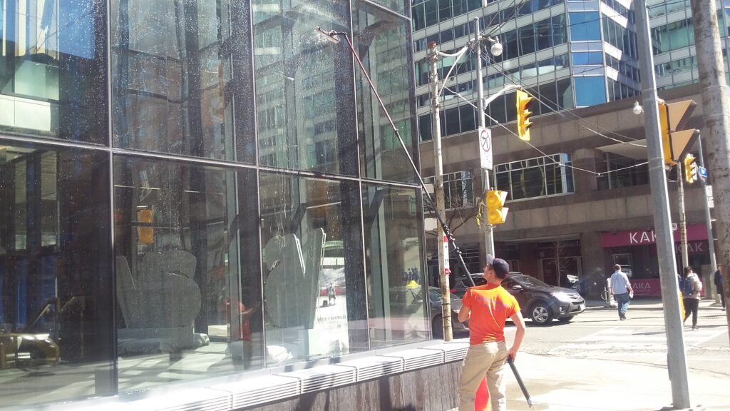 Worker cleaning glass building facade on sunny day