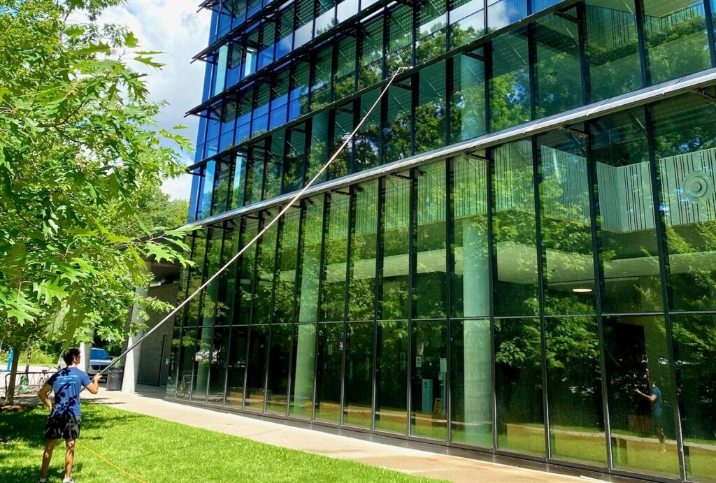 Man cleaning large glass building exterior with hose.