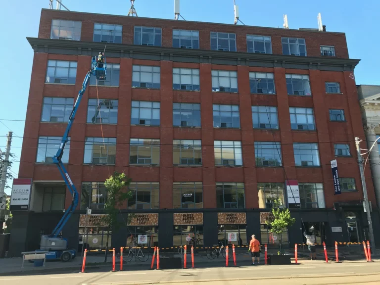 Worker on articulated boom lift cleaning windows on red building.