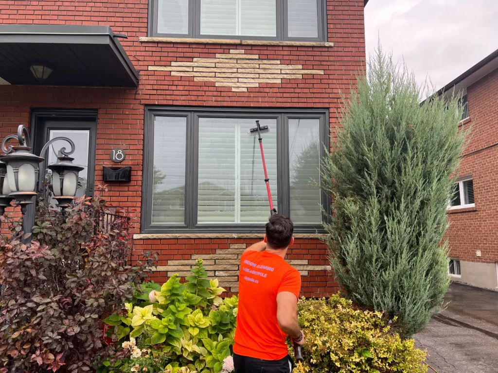 Man cleaning windows with long brush at brick house.