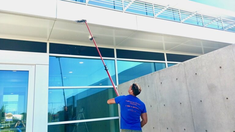 Man using long pole to clean large building exterior surface.