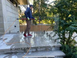 Man cleaning outdoor glass surface with water-fed pole.