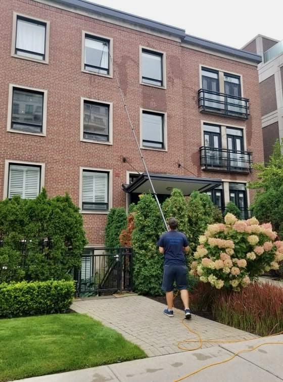 Man cleaning windows with long pole outside brick building.