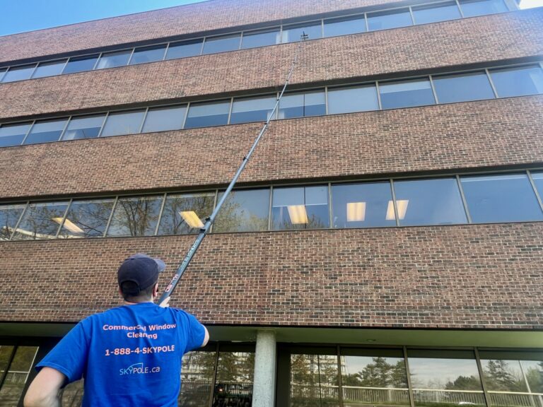 Man cleaning office windows with long pole.