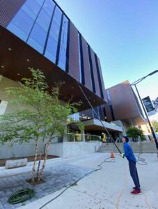 Man cleaning modern building exterior with hose.