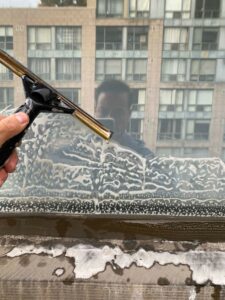 Person cleaning window with squeegee, reflective building background