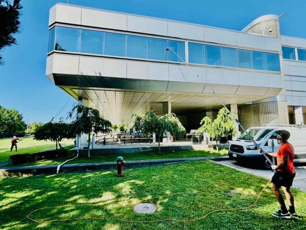 Man power washing modern building exterior on sunny day