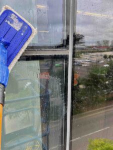 Window cleaning with squeegee on rainy day, urban view, scrub pad