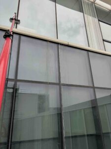 Window cleaning with red pole on glass building exterior, window has stains