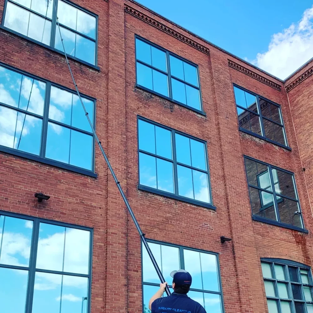 Man cleaning windows on red brick building with long pole.