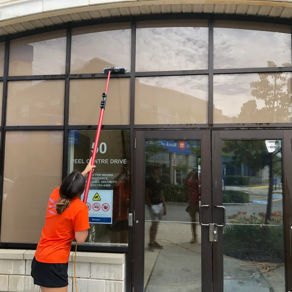 Worker cleaning windows with long-handled squeegee.