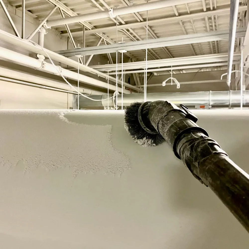 Paint roller applying white paint on industrial ceiling.