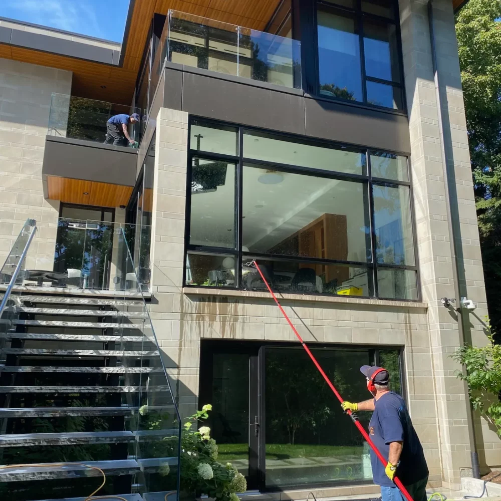 Workers cleaning modern house exterior with equipment.