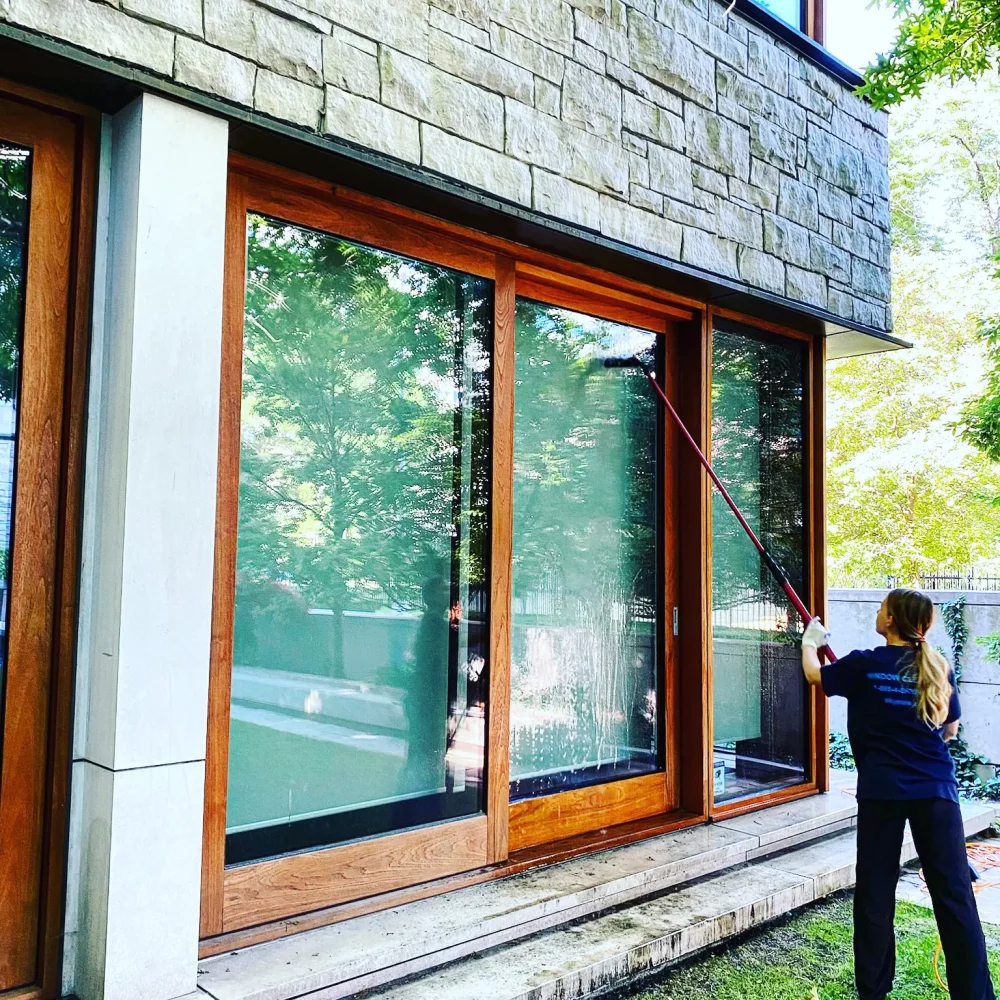 Woman cleaning large windows on modern stone house.