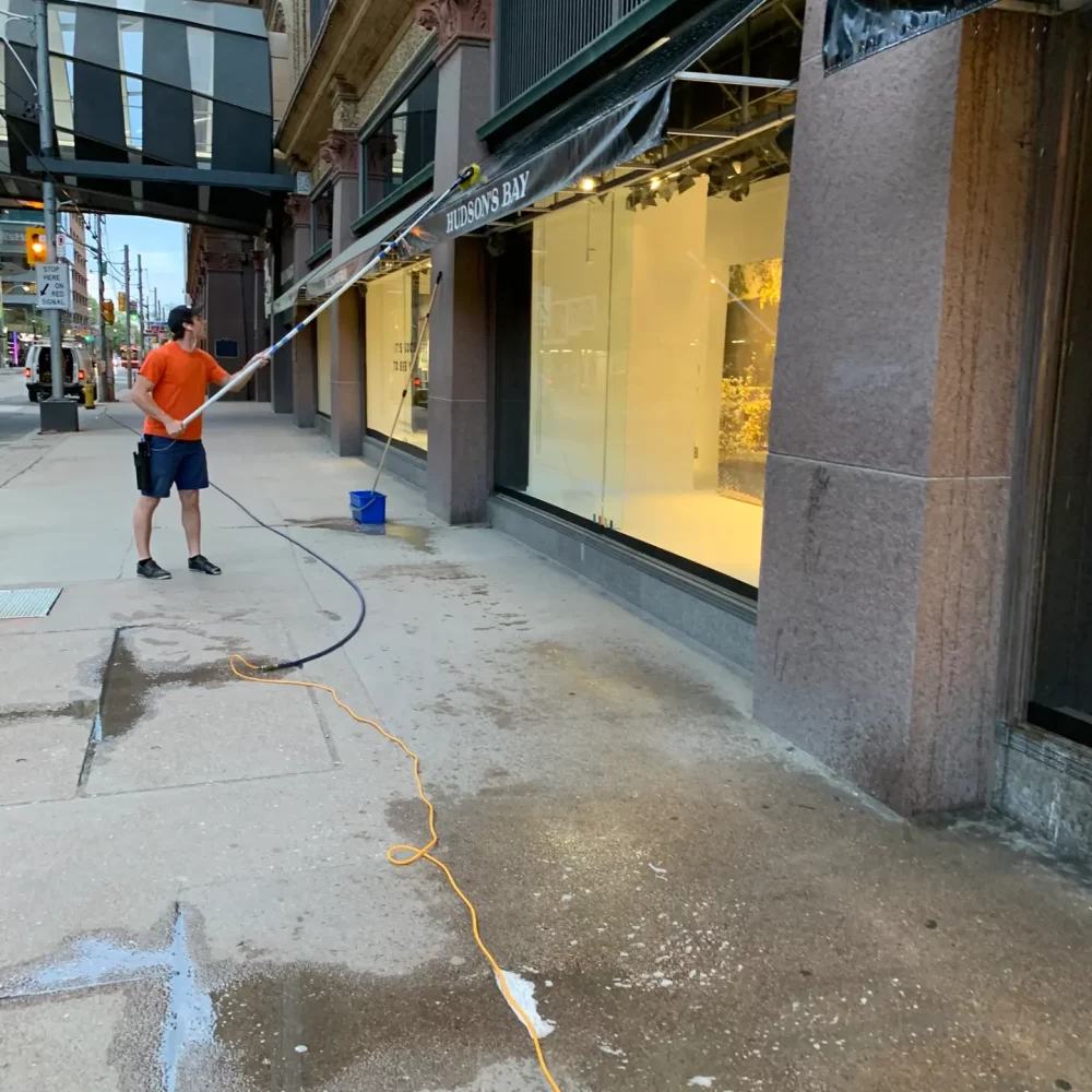Man power-washing sidewalk outside Hudson's Bay store.