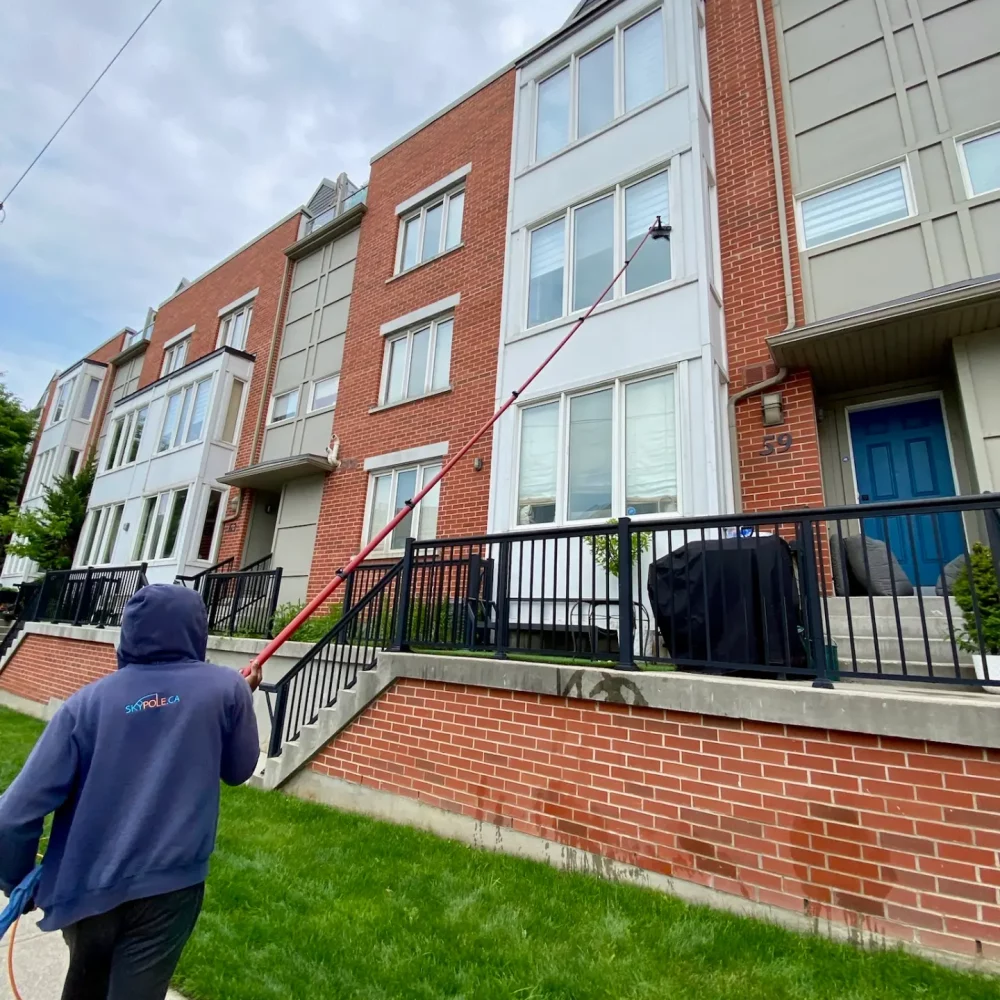 Worker using long pole on residential building exterior.