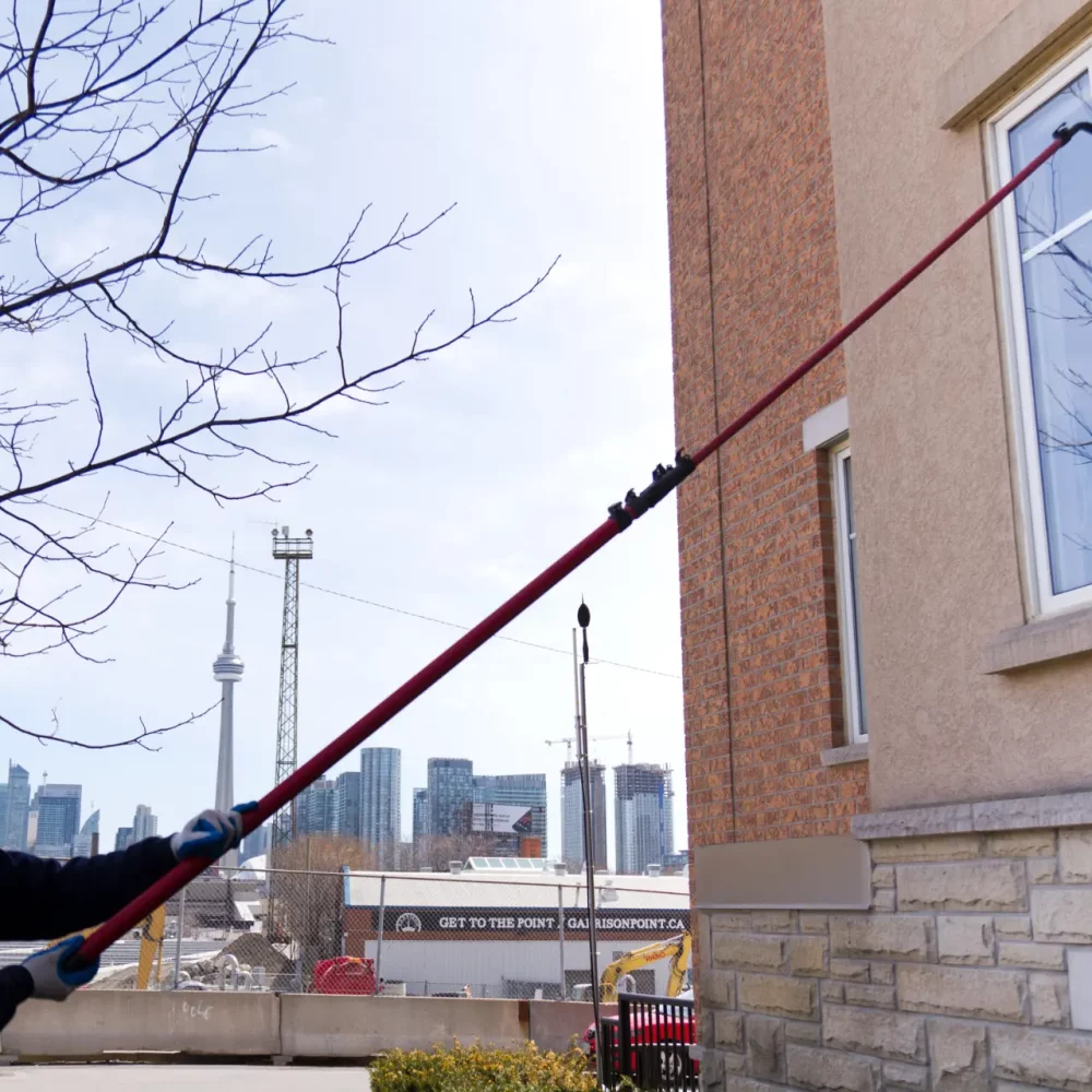 Man cleaning window externally with long pole, city backdrop.