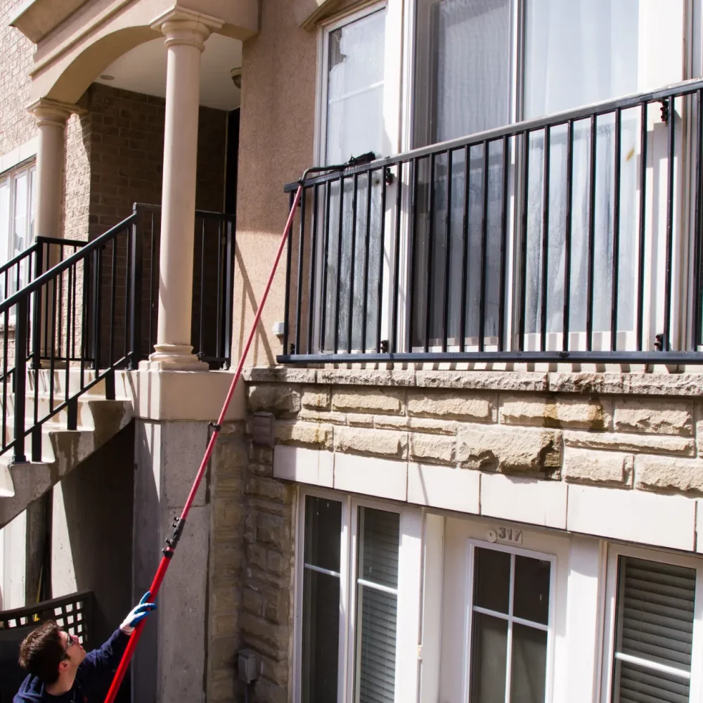 Man cleaning apartment window with long-handled brush.